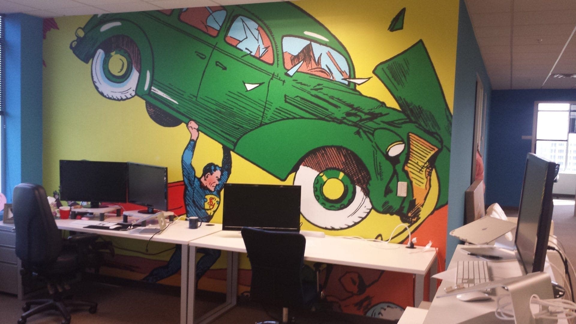 Colorful mural of a vintage car and Superman lifting it, energizing office workspace with creative flair.