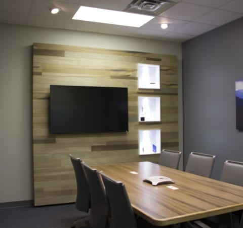 Custom conference room interior with oxidized wooden accent wall with television, table, and hanging nature prints.