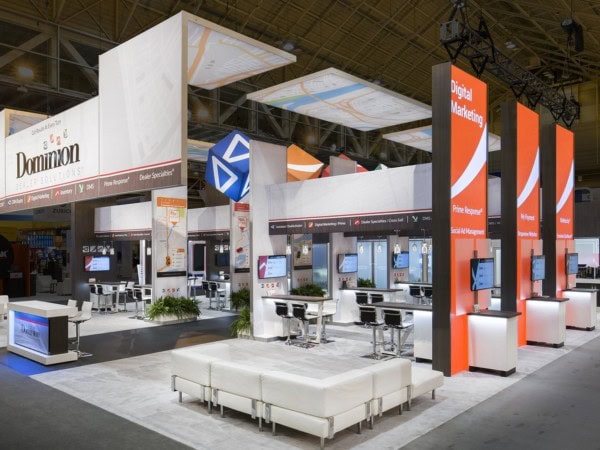 Trade show exhibit with reception desk, suspended ceiling structures, and visitor booths