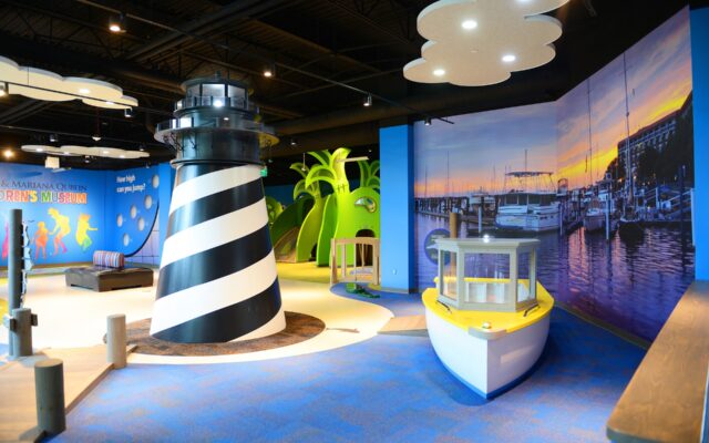 Colorful indoor kids museum with lighthouse and marina-themed murals, interactive play zones, and vibrant lighting.