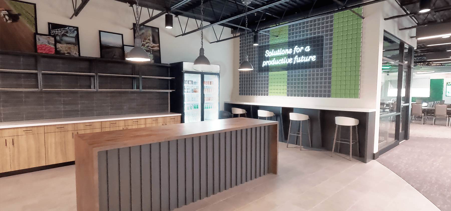 Modern hospitality lounge at the Coastal AgroBusiness Innovation Center with bar table seating, cabinetry, neon-style brand sign, and colorful acoustic wall tiles.