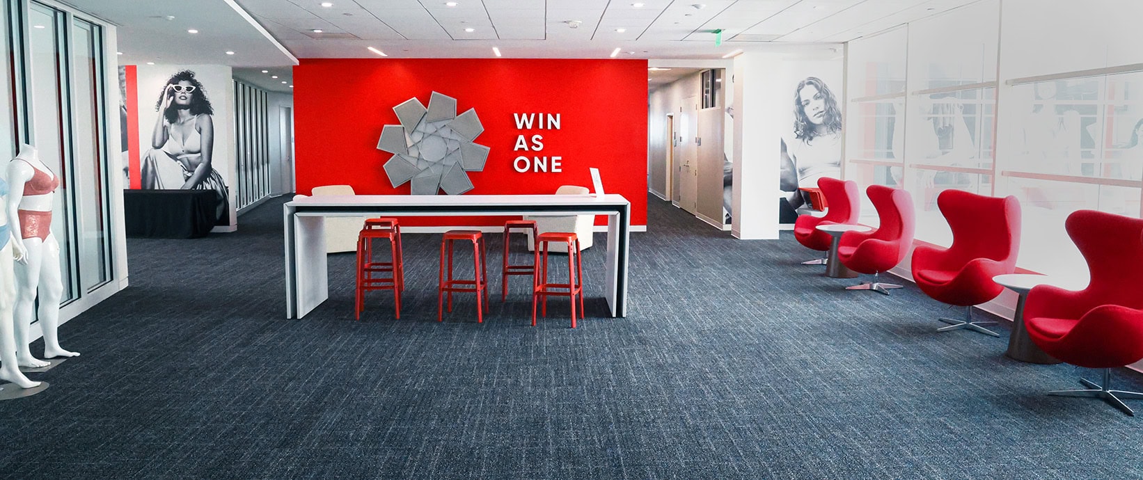 Light-filled room at HanesBrands Park Building featuring the &lsquo;WIN AS ONE&rsquo; 3D mural on the wall. A working table with chairs sits in front of the mural, while additional comfortable seating lines the windows and walls, designed to inspire collaboration, teamwork, and employee engagement.