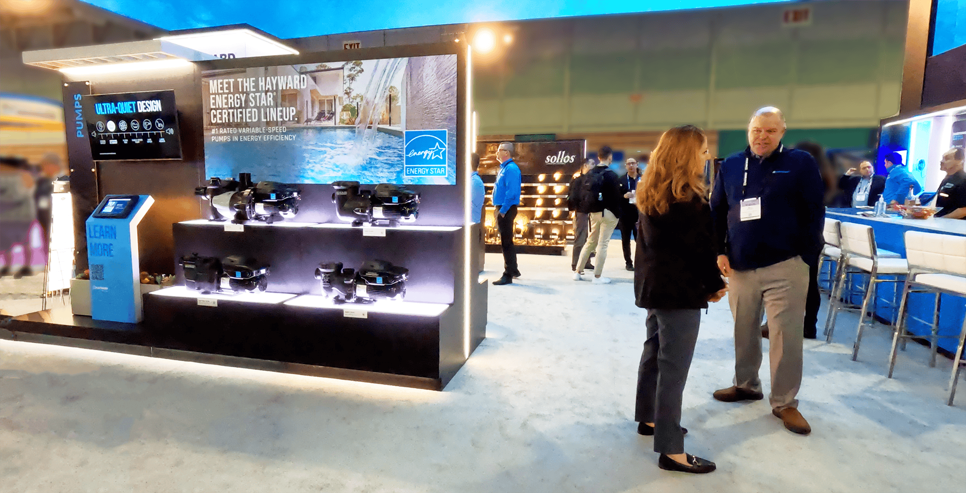 Attendee and Hayward sales representative converse in front of interactive digital monitors and product displays showcasing multiple pool models at the trade show exhibit designed by Holt Experiential.