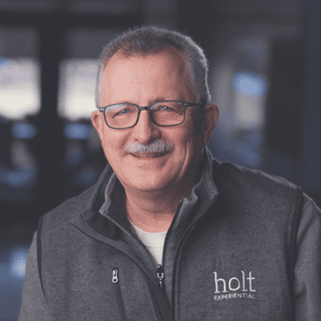 Senior man with glasses smiling in Holt Experiential promotional setting.