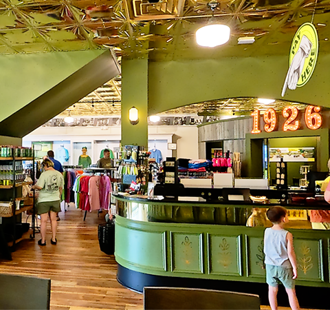 Wide shot of the Mount Olive Pickle Parlor interior showing branded retail displays, apparel, pickle products, a 1926 sign, and the pickle barrel history room.
