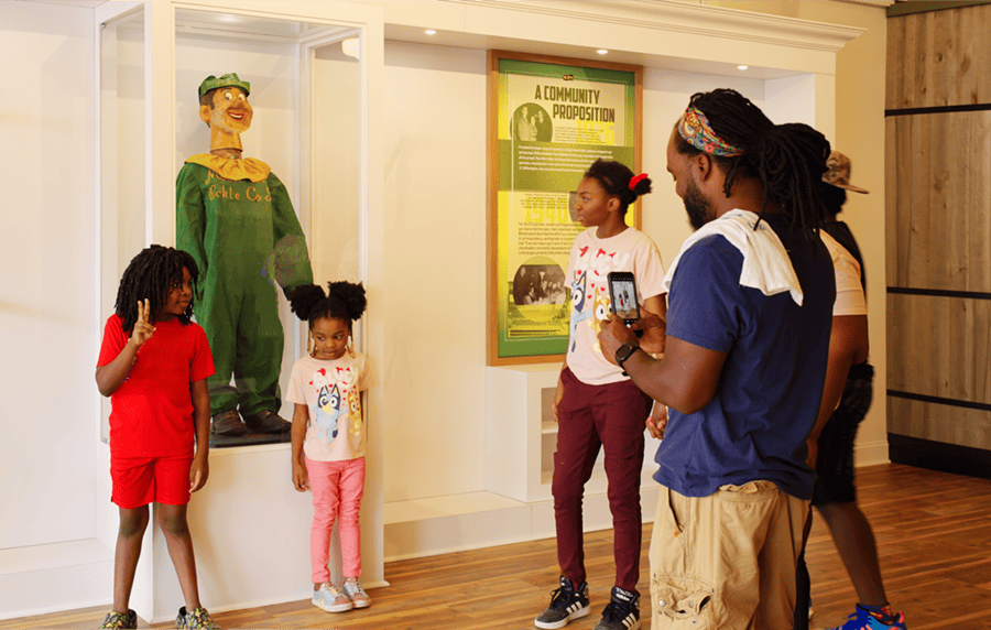 Children posing in front of the historic Mount Olive pickle character with branded signage inside the Pickle Parlor.