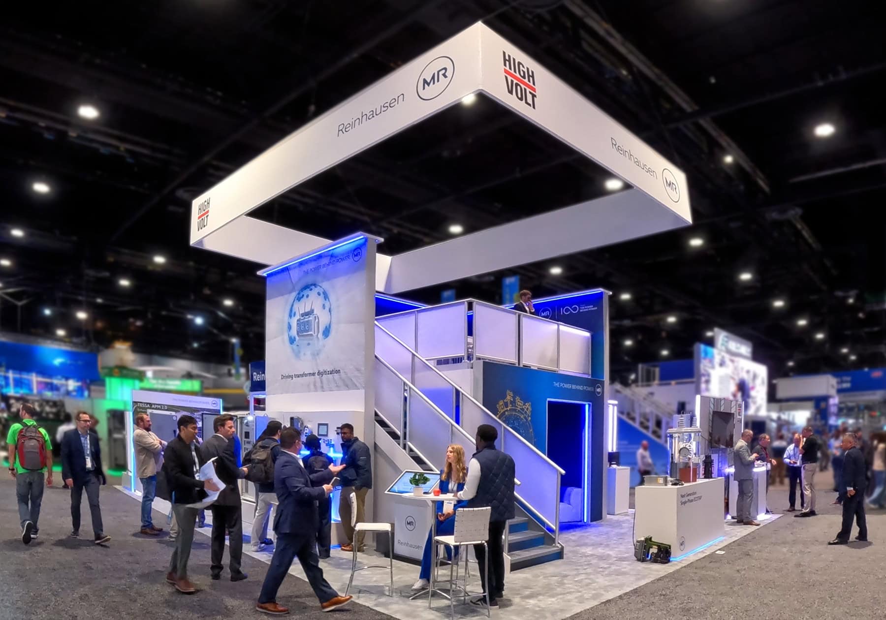 Rear view of Reinhausen's two-story exhibit at IEEE 2026 featuring a private upstairs meeting suite, a casual downstairs meeting lounge, and open seating areas for customer conversations.
